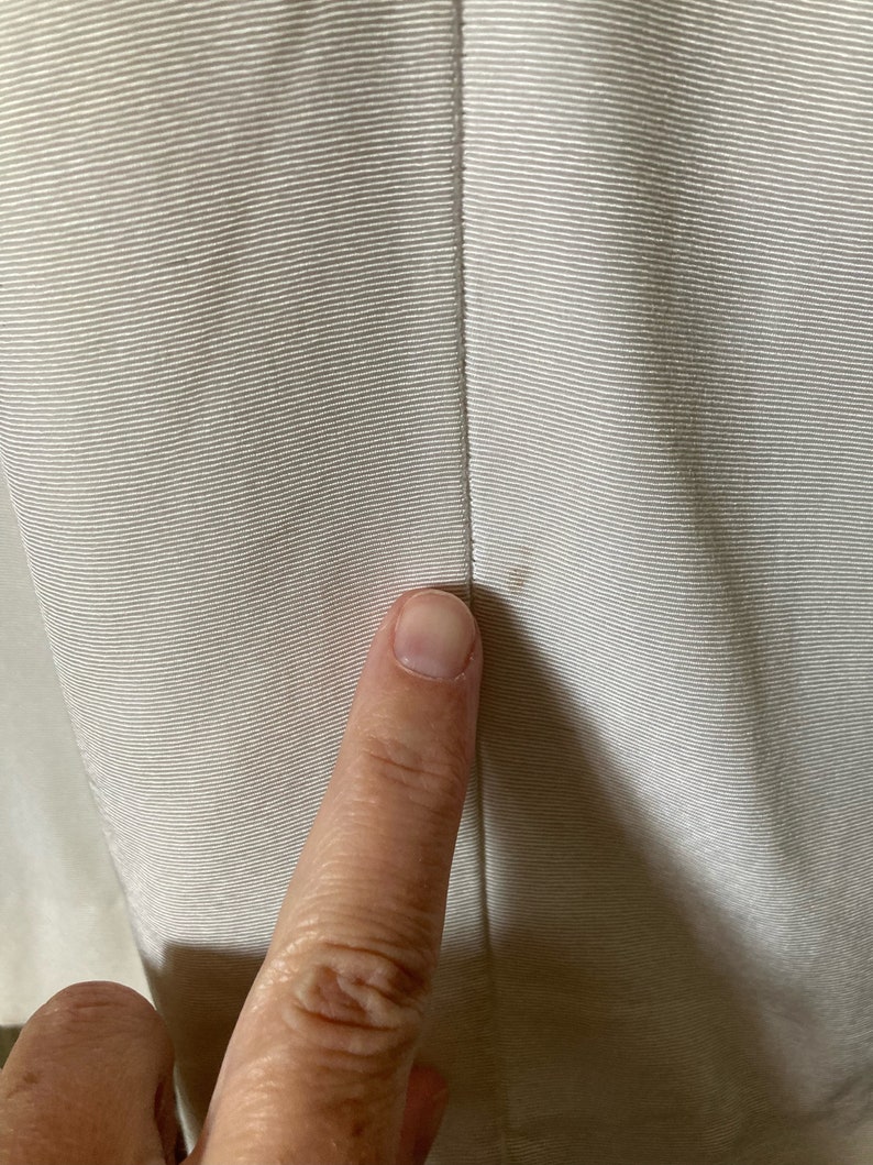May include: A light beige fabric with a fine horizontal ribbed texture and a vertical seam running down the center. A small, faint brown spot is visible on the right side of the seam, indicating a minor imperfection in the material surface.