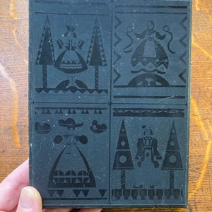 Puede incluir: Grabado en linóleo en blanco y negro con cuatro diseños diferentes. Cada diseño presenta una figura estilizada con un vestido tradicional y un árbol o árboles. Los diseños están separados por un borde negro.