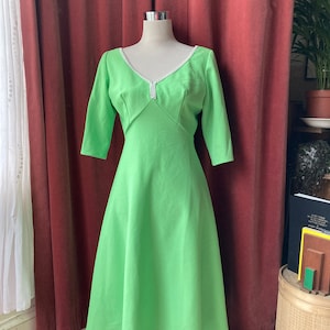 May include: A lime green dress with a white beaded neckline and three-quarter sleeves. The dress has a fitted bodice and a flowing skirt.