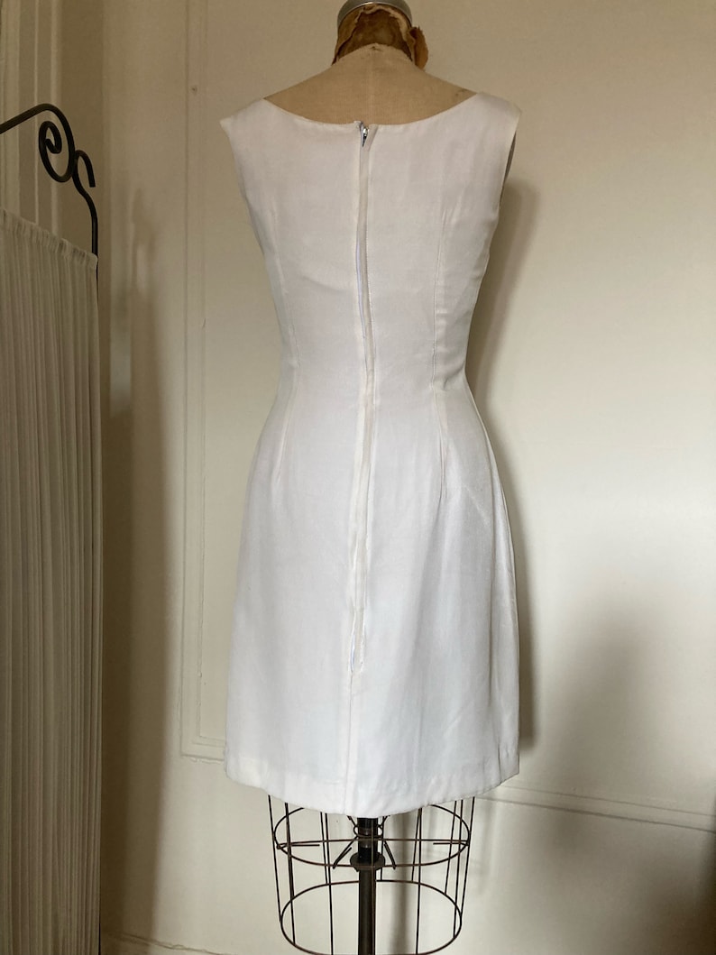 May include: A sleeveless white dress featuring a fitted bodice and a straight skirt. The garment has a high neckline and a long, centered vertical zipper closure running down the back, extending from the neckline to the lower back area.