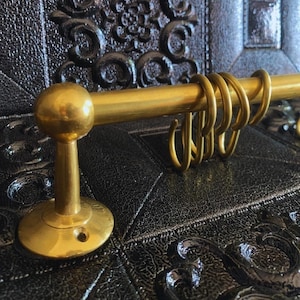 May include: Gold metal kitchen utensil rack with a round base and multiple hooks. The rack is mounted on a black surface.