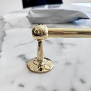 Peut inclure: Un porte-serviettes en or avec un bouton rond sur une surface en marbre blanc.