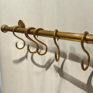 May include: A brass kitchen utensil rack with five hooks. The rack is mounted to a wall and has a round, decorative end cap.