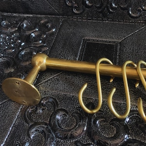 May include: Gold metal kitchen utensil rack with a round base and multiple hooks. The rack is mounted to a black surface.