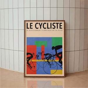 May include: Framed poster titled "LE CYCLISTE" with a vintage design. The artwork features cyclists in black silhouettes against a backdrop of red, blue, and green geometric shapes. The poster is in a wooden frame.