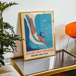 May include: A framed poster with a retro design featuring a woman diving into blue water with white bubbles. The poster has the text "ESPLORA ACQUE CRISTALLINE COSTIERA AMALFITANA" in red, blue, and white.