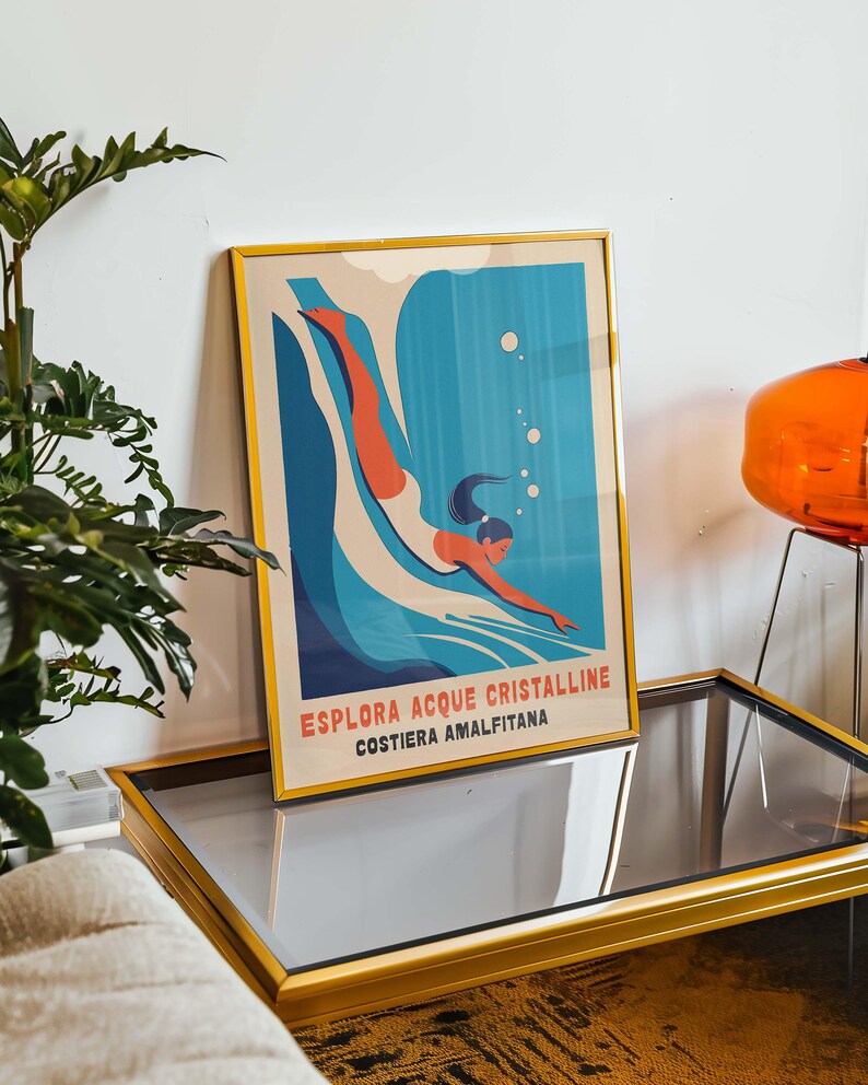 May include: A framed poster with a retro design featuring a woman diving into blue water with white bubbles. The poster has the text "ESPLORA ACQUE CRISTALLINE COSTIERA AMALFITANA" in red, blue, and white.