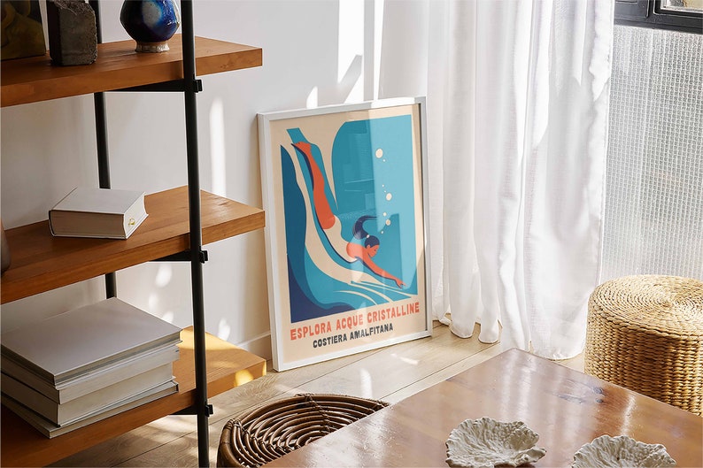 May include: A framed poster with a blue and white illustration of a person diving into water. The poster has the text "Esplora Acque Cristalline Costiera Amalfitana".