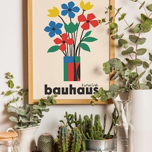 Pu&ograve; includere: Una stampa incorniciata con un'illustrazione colorata di fiori in un vaso. La stampa ha il testo "botanisch bauhaus" in lettere nere. La stampa &egrave; su uno scaffale con piante in vaso e una bottiglia di vetro.