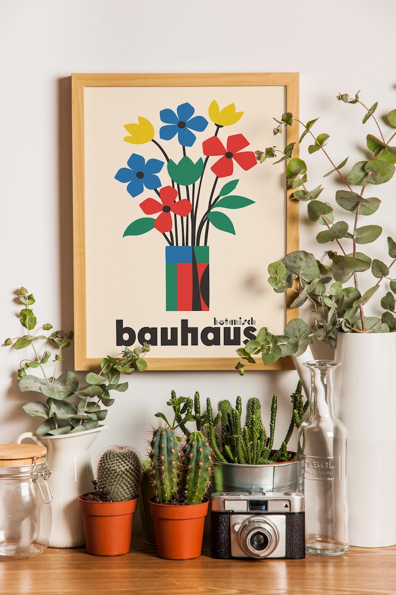 Pu&ograve; includere: Una stampa incorniciata con un'illustrazione colorata di fiori in un vaso. La stampa ha il testo "botanisch bauhaus" in lettere nere. La stampa &egrave; su uno scaffale con piante in vaso e una bottiglia di vetro.