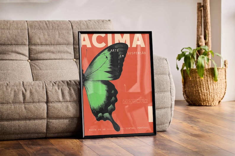 May include: Framed art print with a green and black butterfly on a red backdrop. The print features the word "ACIMA" in cream. The artwork is displayed on a grey sofa. The print is in a black frame.