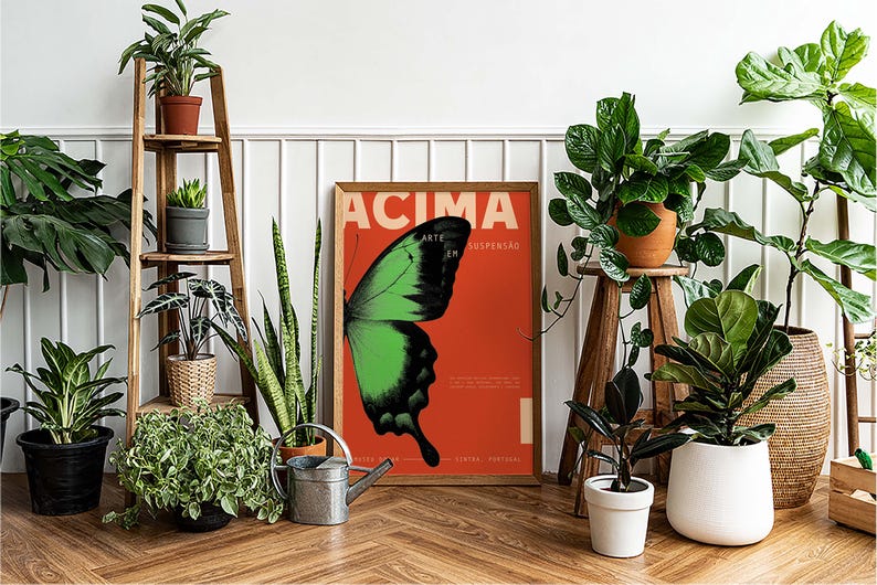 May include: A framed poster featuring a green and black butterfly wing on a red backdrop, with the word "ACIMA" at the top. The poster is surrounded by potted plants, including a wooden plant stand and a watering can.