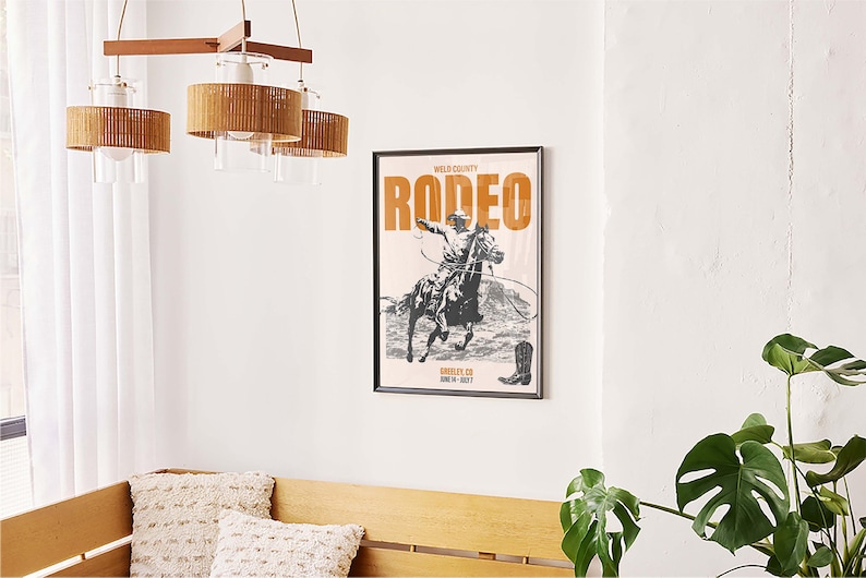 Pode incluir: Um p&ocirc;ster preto e branco com o texto "Wild County Rodeo" em letras laranja. O p&ocirc;ster apresenta um caub&oacute;i montando um cavalo. O p&ocirc;ster est&aacute; emoldurado em uma moldura preta.
