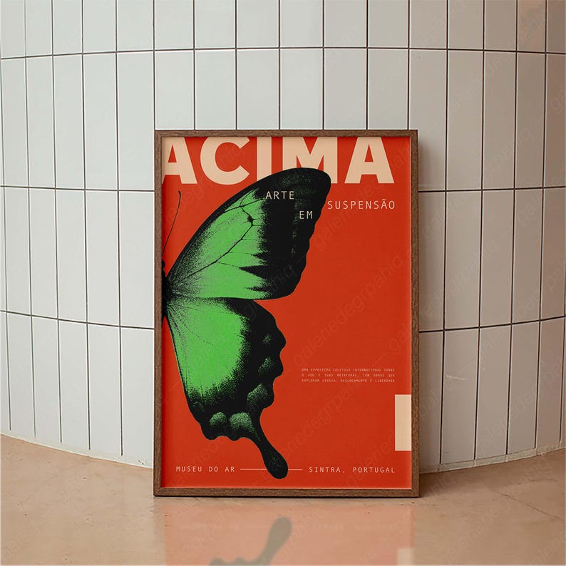 May include: A framed poster featuring a green and black butterfly wing on a red background. The poster has the word "ACIMA" in white, with Portuguese text. The poster is displayed in a room with white tiles.