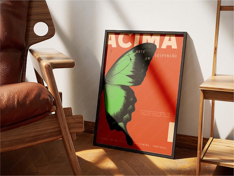 May include: Framed poster with a butterfly wing design in green and black against a red background. The poster has the word "ACIMA" at the top and other text. The poster is leaning against a white wall.