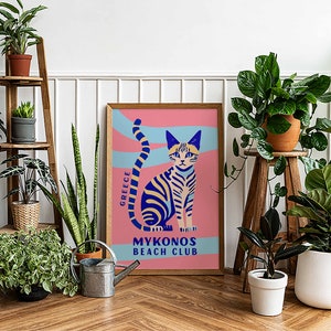 May include: A colorful poster with a blue and yellow striped cat sitting on a pink background. The poster says "Greece" and "Mykonos Beach Club".