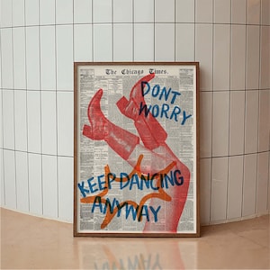 Puede incluir: Una impresión artística enmarcada con un fondo de periódico, botas rojas y las palabras "DON'T WORRY KEEP DANCING ANYWAY" en azul y naranja. La impresión tiene un marco de madera y se muestra contra una pared de azulejos blancos.