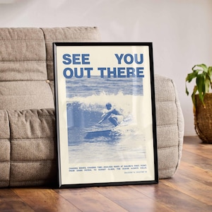 K&ouml;nnte beinhalten: Ein blaues und wei&szlig;es Poster mit dem Text "See You Out There" und einem Foto eines Surfers, der auf einer Welle reitet. Das Poster ist schwarz gerahmt und h&auml;ngt an einer Wand.