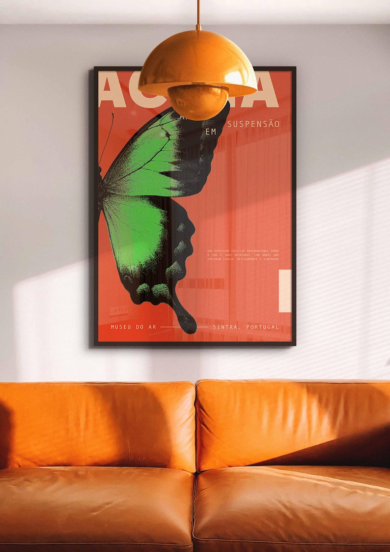 May include: A framed poster featuring a green and black butterfly design on a red backdrop. The poster has Portuguese text, including "Museu do Ar" and "Sintra, Portugal". An orange pendant light hangs above an orange leather sofa.