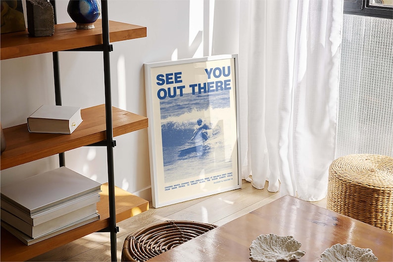 K&ouml;nnte beinhalten: Ein wei&szlig;er gerahmter Poster mit blauem Text, der "See You Out There" lautet, und einer blauen und wei&szlig;en Illustration einer Person beim Surfen. Der Poster h&auml;ngt an einer wei&szlig;en Wand.