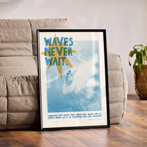 May include: Framed art print with the text "WAVES NEVER WAIT" in blue and yellow. The image depicts a surfer riding a wave. The print is in a black frame and is leaning against a gray sofa.