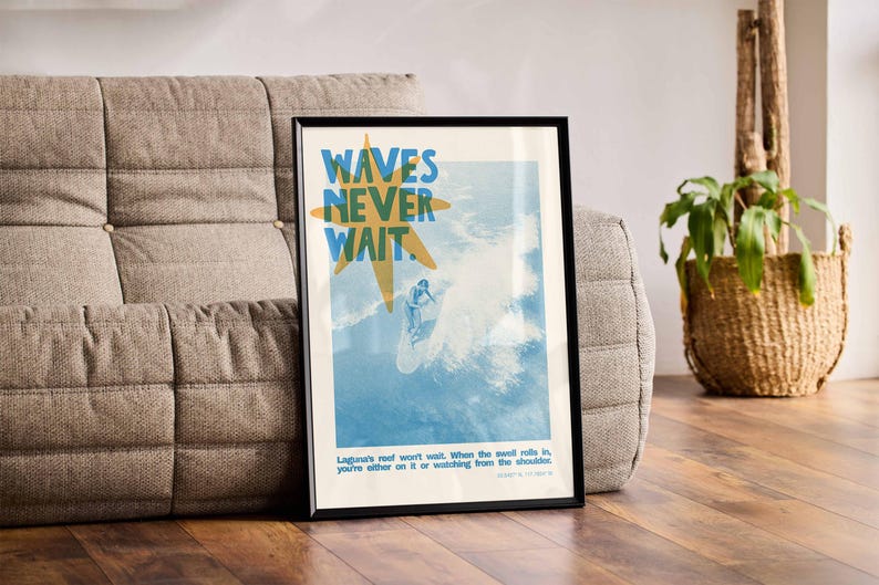 May include: Framed art print with the text "WAVES NEVER WAIT" in blue and yellow. The image depicts a surfer riding a wave. The print is in a black frame and is leaning against a gray sofa.