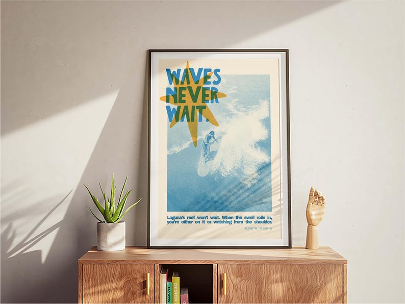 May include: Framed art print with a surfing theme. The poster features the text "WAVES NEVER WAIT" in blue and yellow, with a surfer riding a wave. The print includes additional text at the bottom. The artwork is displayed on a wooden cabinet.
