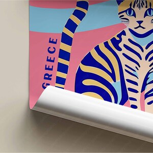 May include: A colorful poster with a blue and yellow striped cat on a pink background. The poster has the word "GREECE" written vertically in blue letters.