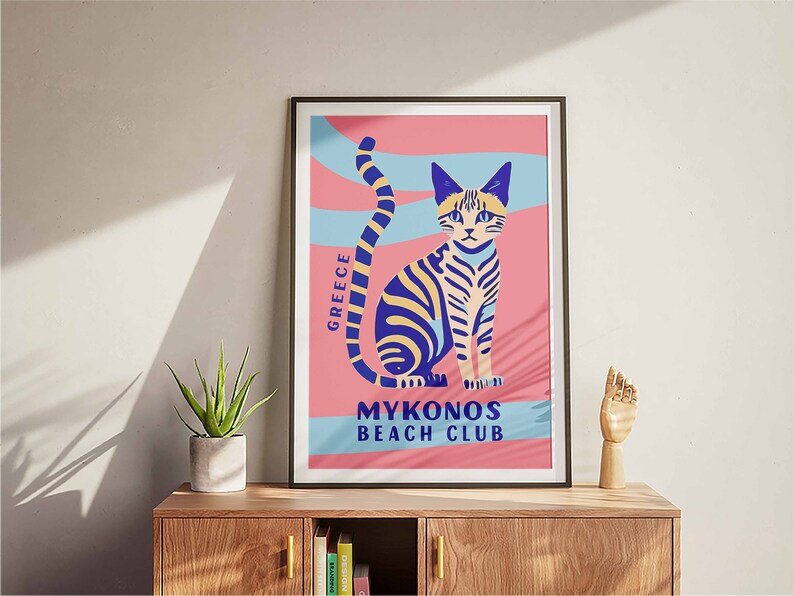 May include: A pink and blue poster with a stylized illustration of a cat. The poster has the text "GREECE" and "MYKONOS BEACH CLUB".