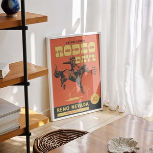 K&ouml;nnte beinhalten: Ein gerahmtes Poster mit einem Vintage-Design, das f&uuml;r die "Washoe County Rodeo Days" in Reno, Nevada wirbt. Das Poster zeigt einen Cowboy, der ein wildes Pferd reitet, mit dem Text "August 23-29" und "12th Annual" in der rechten unteren Ecke.