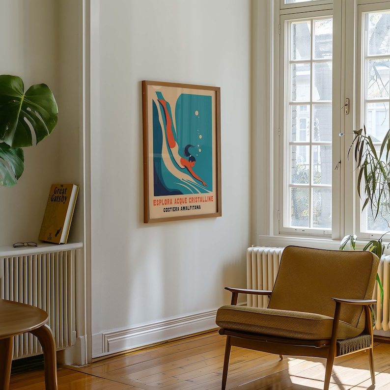 May include: A vintage-style poster with a woman diving into blue water. The poster is framed in wood and has the text "ESPLORA ACQUE CRISTALLINE COSTIERA AMALFITANA" in white letters.