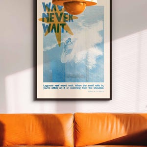 May include: A framed poster with the words "WAV NEVER WAIT" in blue and yellow, depicting a surfer riding a wave. The poster is hanging above an orange leather couch, with an orange pendant light above.