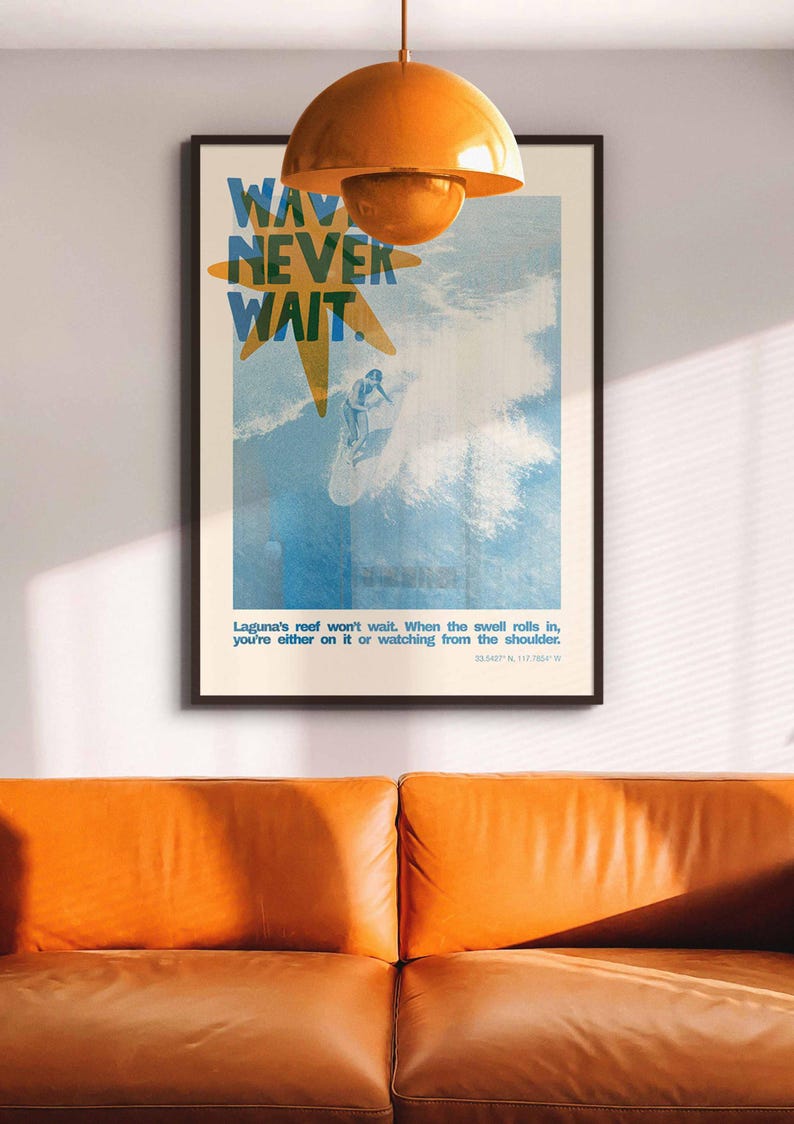 May include: A framed poster with the words "WAV NEVER WAIT" in blue and yellow, depicting a surfer riding a wave. The poster is hanging above an orange leather couch, with an orange pendant light above.