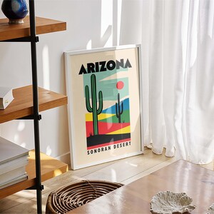 Może przedstawiać: Biały plakat w ramie z tekstem "Arizona Sonoran Desert" i kolorową ilustracją kaktusa z czerwonym słońcem w tle.