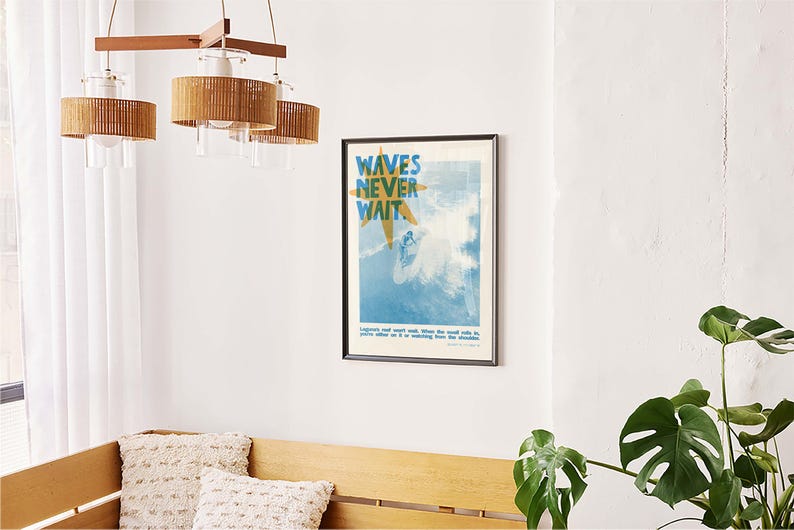 May include: A framed poster with the text "WAVES NEVER WAIT" in blue and yellow, depicting a surfer in the ocean. The poster is hanging on a white wall. A wooden bench with two decorative pillows is below the poster. A wooden and rattan chandelier hangs above.