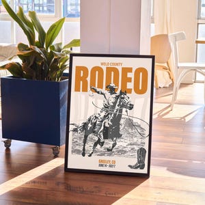 Pode incluir: Um p&ocirc;ster emoldurado em preto com uma ilustra&ccedil;&atilde;o de estilo vintage de um cowboy montando um cavalo. O p&ocirc;ster tem o texto "WELD COUNTY RODEO GREELEY, CO JUNE 14 - JULY 7" em laranja e preto.