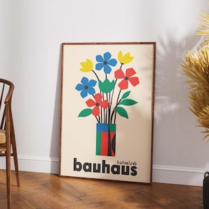 Pu&ograve; includere: Un poster incorniciato con un'illustrazione colorata di un mazzo di fiori in un vaso. I fiori sono rossi, blu, gialli e verdi. Il testo "bauhaus botanisch" &egrave; in fondo al poster.