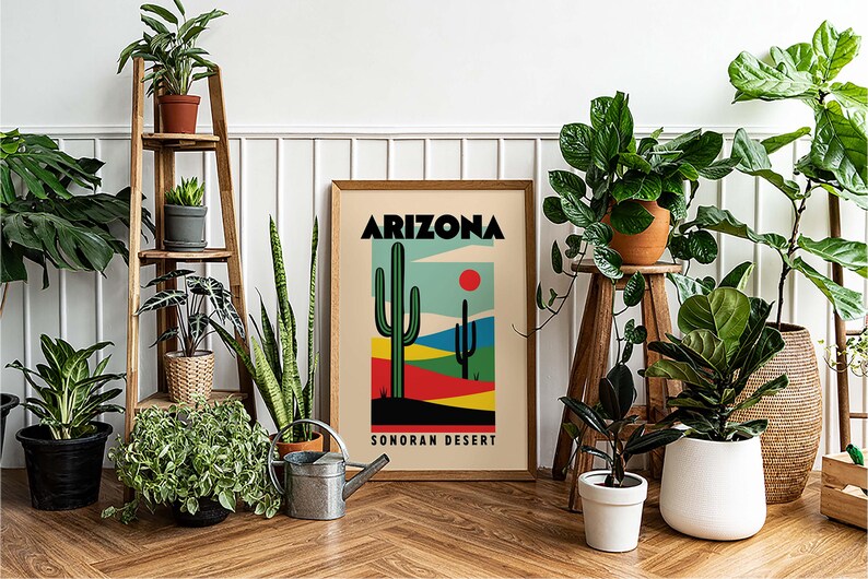 Może przedstawiać: Ramka z plakatem z tekstem "ARIZONA SONORAN DESERT" i kolorową ilustracją dw&oacute;ch kaktus&oacute;w i czerwonego słońca. Plakat jest otoczony doniczkowymi roślinami, w tym wężownicą, figowcem lirolistnym i gumowcem.