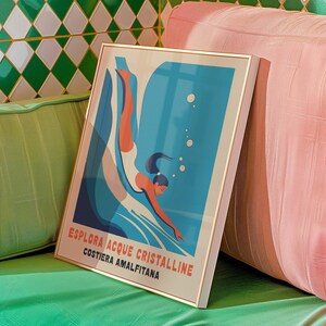 May include: A framed poster with a blue and white illustration of a person diving into water. The poster has the text "Esplora Acque Cristalline Costiera Amalfitana" in red and white.
