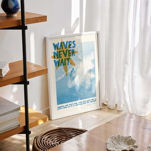 May include: A framed poster with the text "WAVES NEVER WAIT" in blue and yellow, depicting a surfer on a wave. The poster is leaning against a wall near a wooden table and a woven basket. A wooden shelf with books and decorative items is visible.