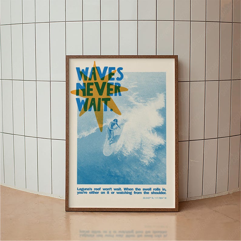 May include: Framed poster with a surfing theme. The poster features the text "WAVES NEVER WAIT" in blue and yellow, with an illustration of a surfer riding a wave. The bottom of the poster includes additional text. The frame is brown.