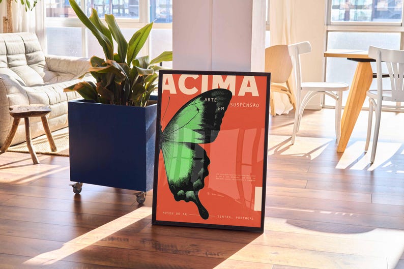 May include: A framed poster with a butterfly wing design in green and black on a red backdrop. The poster includes the word "ACIMA" and other text. The poster is displayed on a wooden floor.
