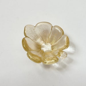 May include: A small, gold-colored glass dish shaped like a flower with five petals.