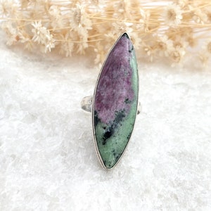 Puede incluir: Un anillo de plata con una gran piedra preciosa ovalada de color verde y rosa. La piedra preciosa tiene un patrón de mármol verde, rosa y negro.
