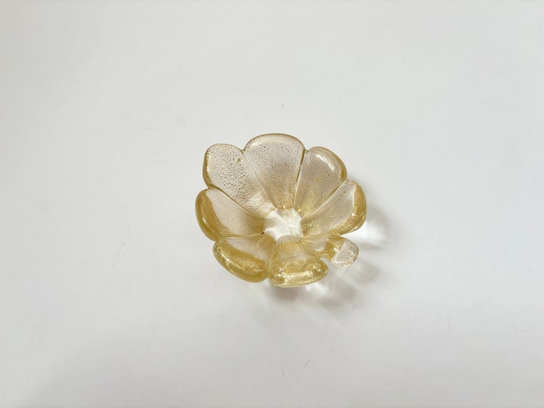 May include: A small, gold-colored glass dish shaped like a flower with five petals.
