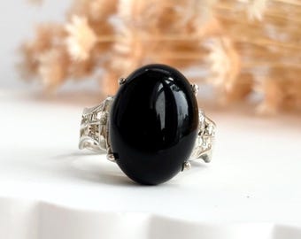 Könnte beinhalten: Ein silberner Ring mit einem großen, ovalen schwarzen Edelstein. Der Ring hat ein filigranes, kompliziertes Design.