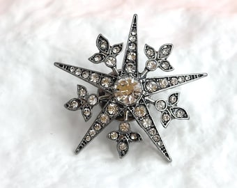 Spilla vintage da bavero color argento con fiocco di neve/stella polare e strass, in stile bigiotteria.
