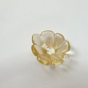 May include: A small, gold-colored glass dish shaped like a flower with five petals.