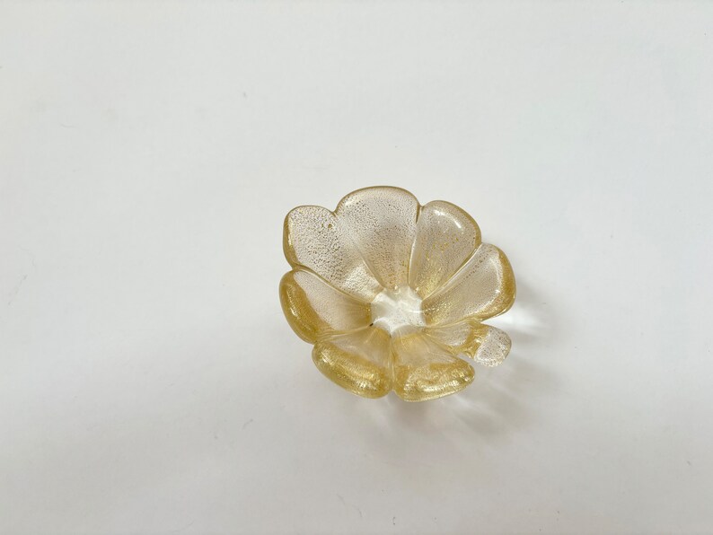 May include: A small, gold-colored glass dish shaped like a flower with five petals.