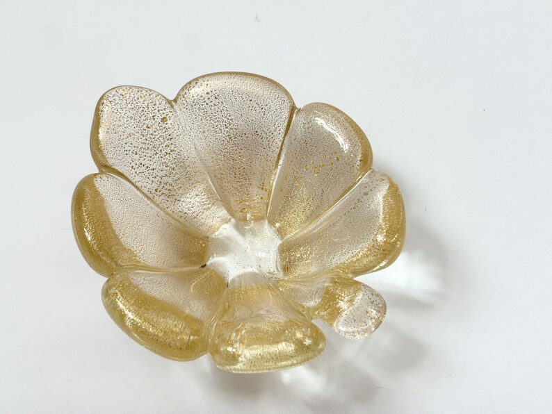 May include: A gold and white glass bowl shaped like a flower with five petals.